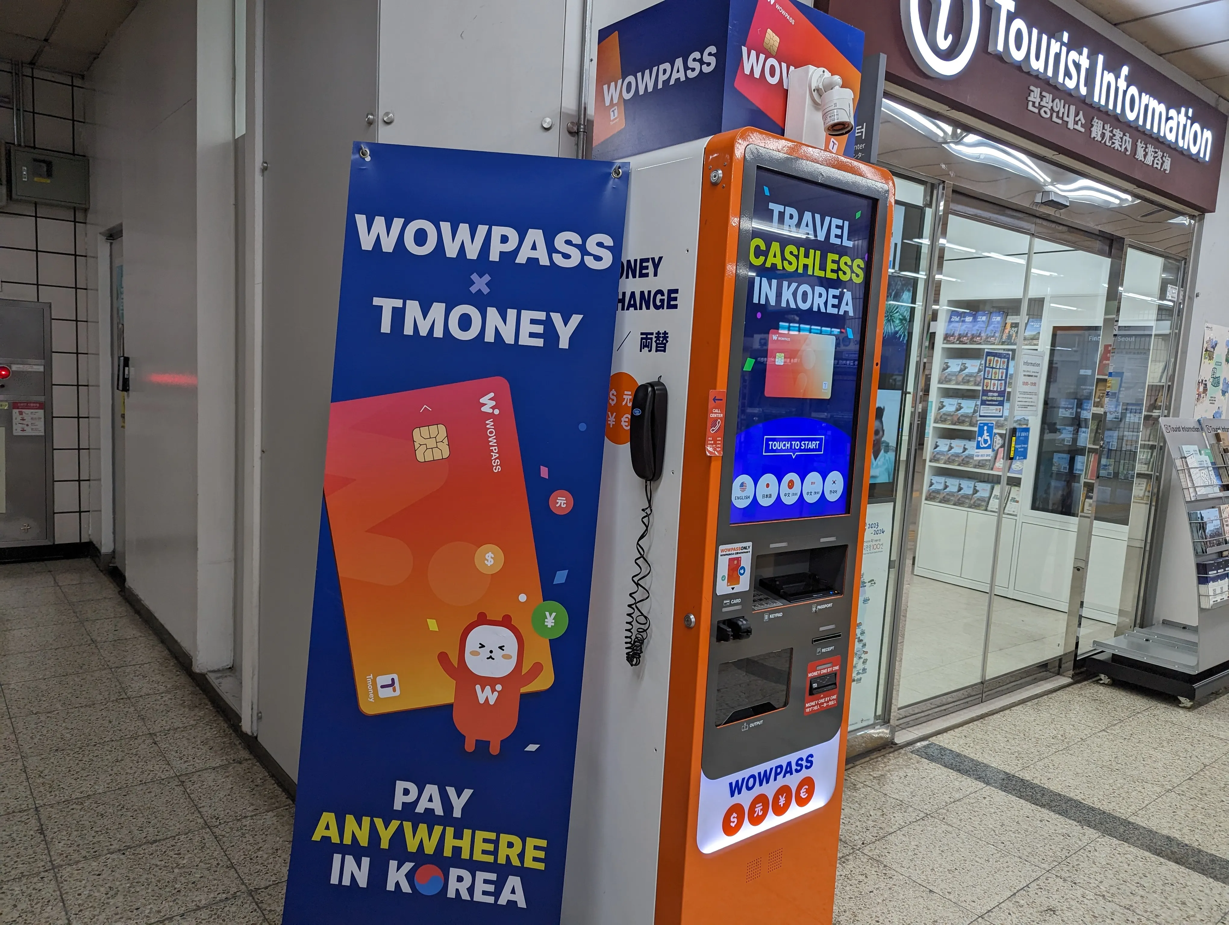 WOWPASS 與 TMONEY 的專用機台。「TRAVEL CASHLESS IN KOREA」橘色機殼與旁邊的 WOWPASS × TMONEY 介紹面板。